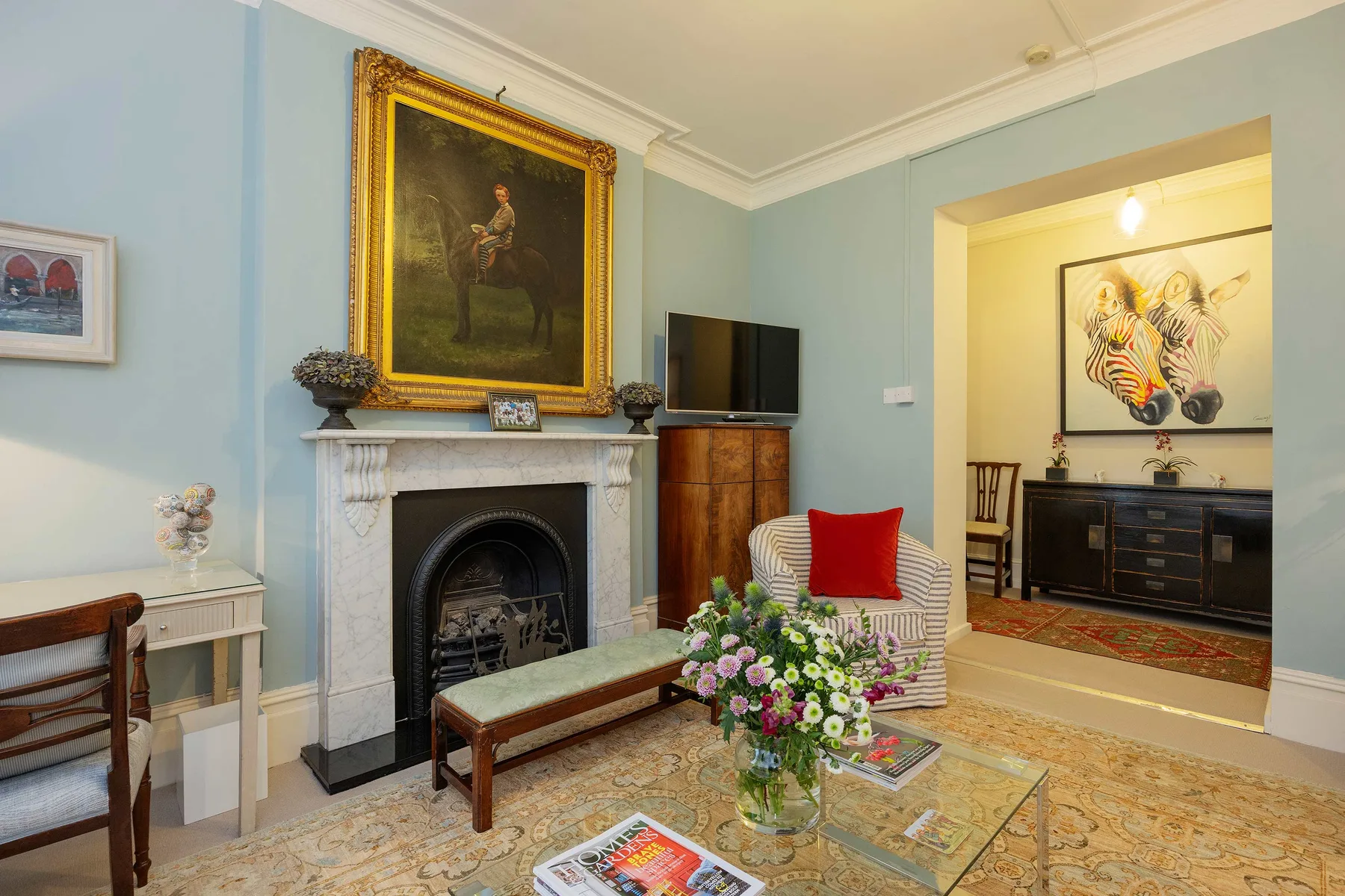 A living room with a fireplace, seating, and a colorful floral arrangement.