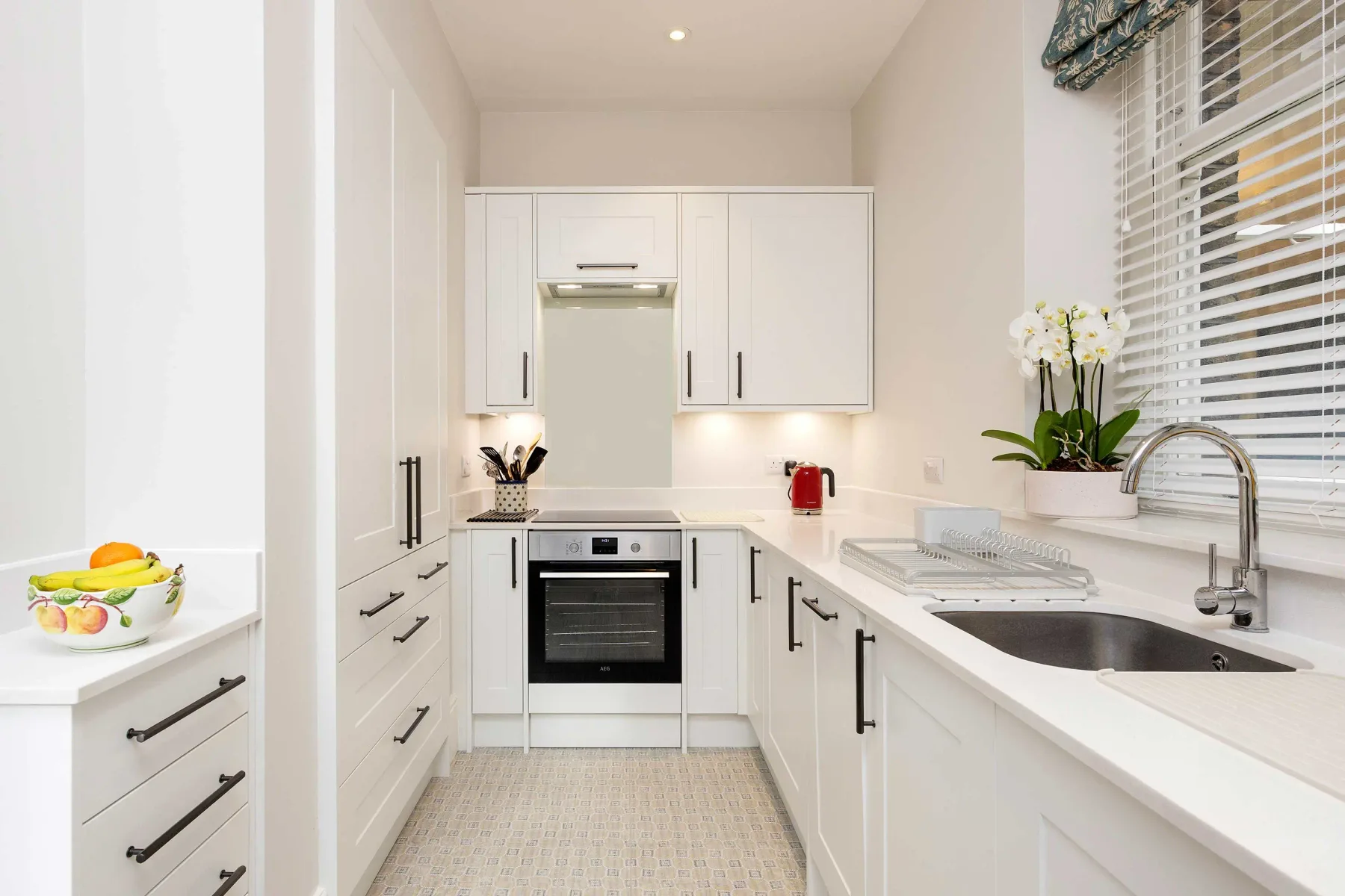 A bright white kitchen with cabinets, a built-in oven, and a sink beneath the window.