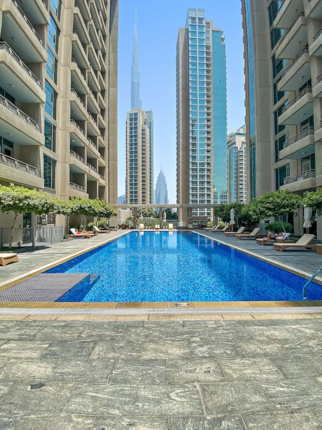 Una piscina está entre altos edificios de apartamentos bajo un cielo azul despejado.