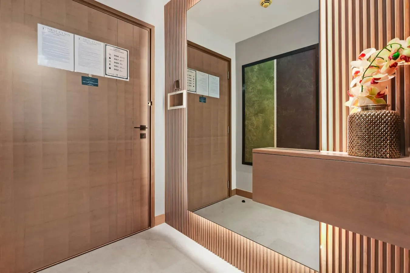 Una entrada interior revestida de madera, con puertas y un jarrón decorativo sobre un mostrador.
