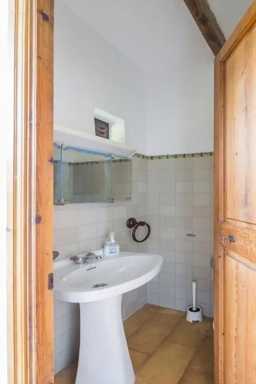 A tiled bathroom has a white pedestal sink and a wall-mounted mirror.