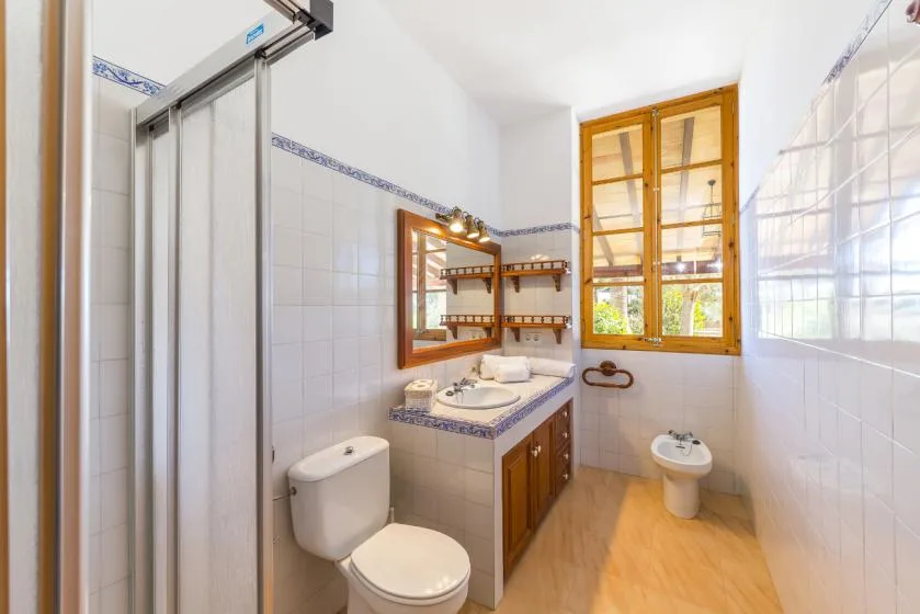 A bright bathroom with a sink, toilet, and a wooden-framed window.