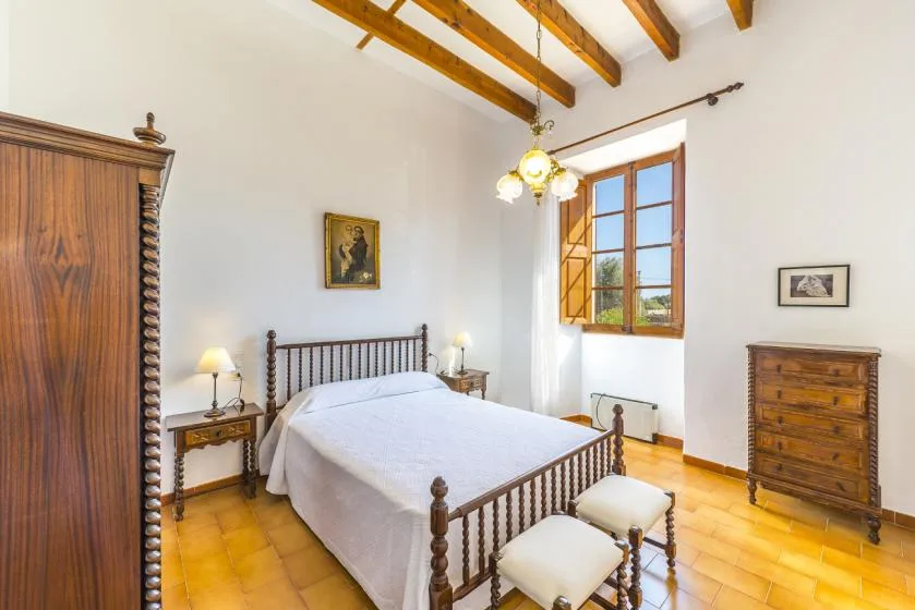 A bright bedroom with a metal-framed bed beneath exposed wooden ceiling beams.