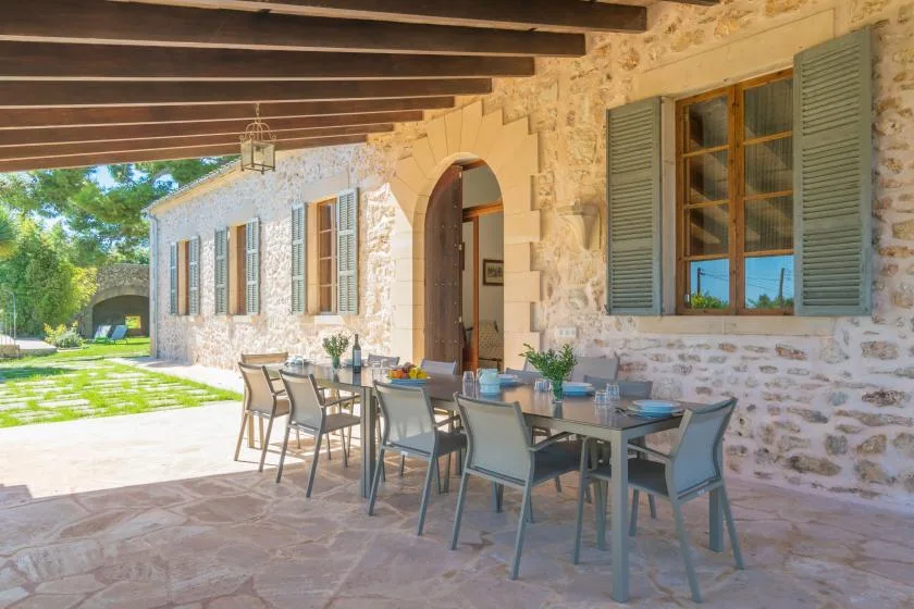 A stone house patio has outdoor seating beneath a wooden pergola.