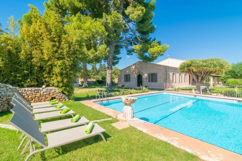 An outdoor swimming pool beside a low house, with loungers on the lawn.