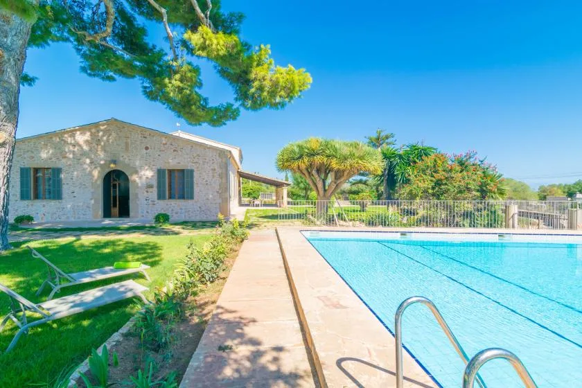 A swimming pool beside a stone building, with lounge seating on the lawn.