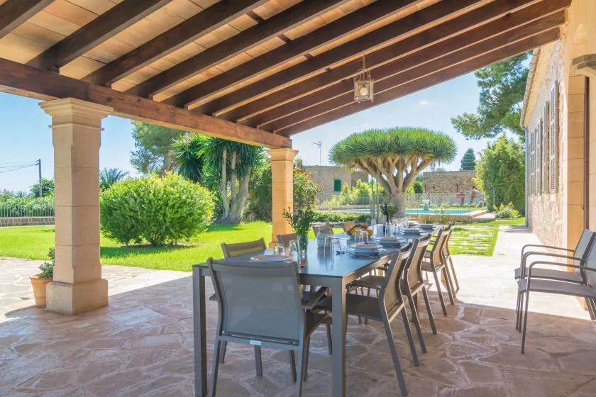 A covered outdoor dining patio overlooks a green garden and swimming pool.