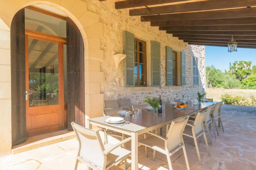 A covered outdoor dining area with a long table and seating beside a stone wall.