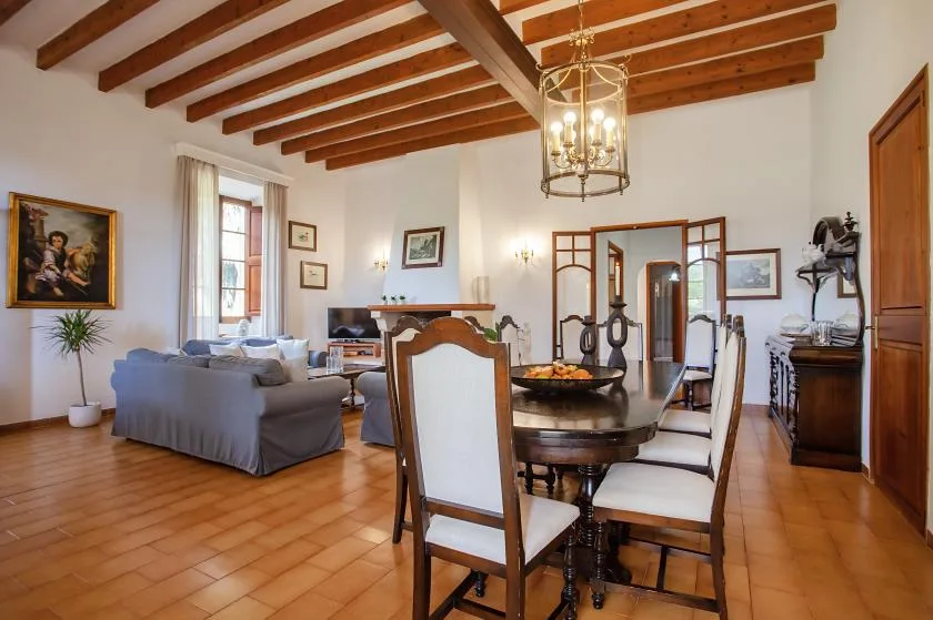 A dining and living room with a wooden table, seating, and exposed ceiling beams.