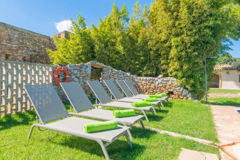 A grassy outdoor lounging area with reclining seating beside stone walls and trees.