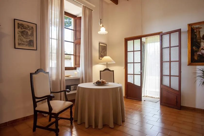 A dining area with a round table set beside tall windows and wooden doors.