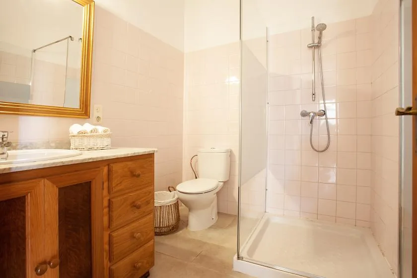 A bathroom with a wooden vanity, toilet, and glass-enclosed shower.