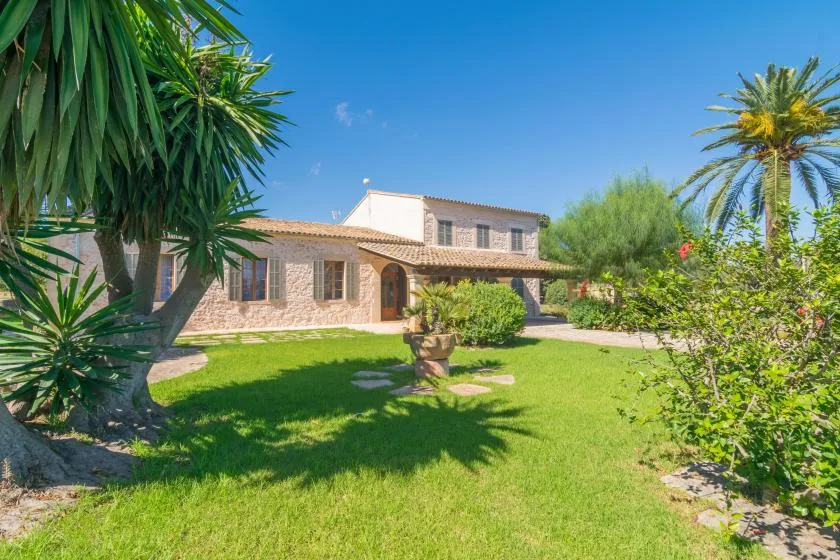 A stone house faces a green lawn with palm trees and shrubs.