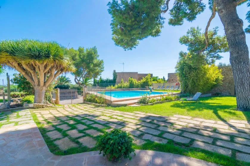 A landscaped garden surrounds an outdoor swimming pool, with trees and paved paths.