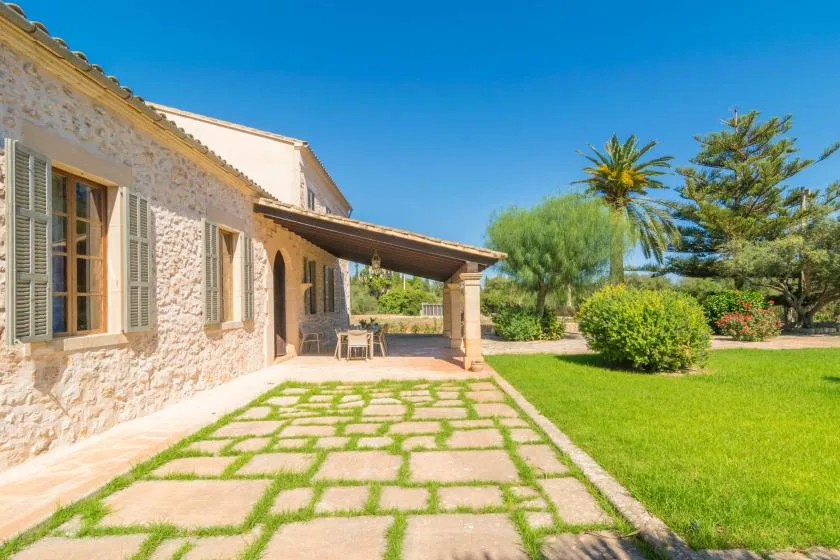 A stone house opens onto a paved patio beside a green lawn.