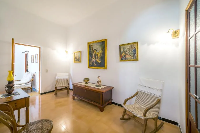 A bright sitting room with wooden seating, framed paintings, and a polished floor.