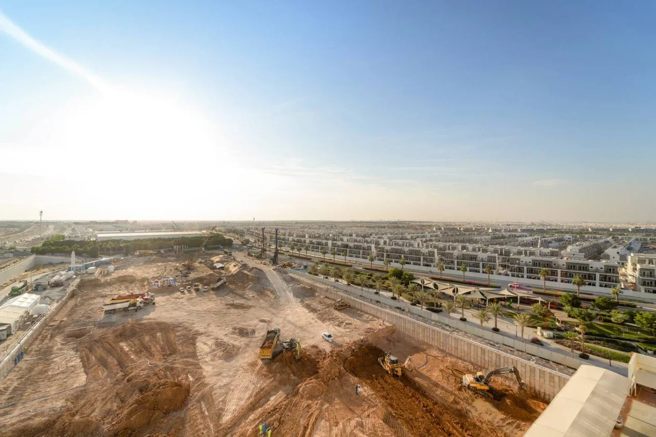 A wide view of a construction site with earthmoving equipment and buildings beyond.