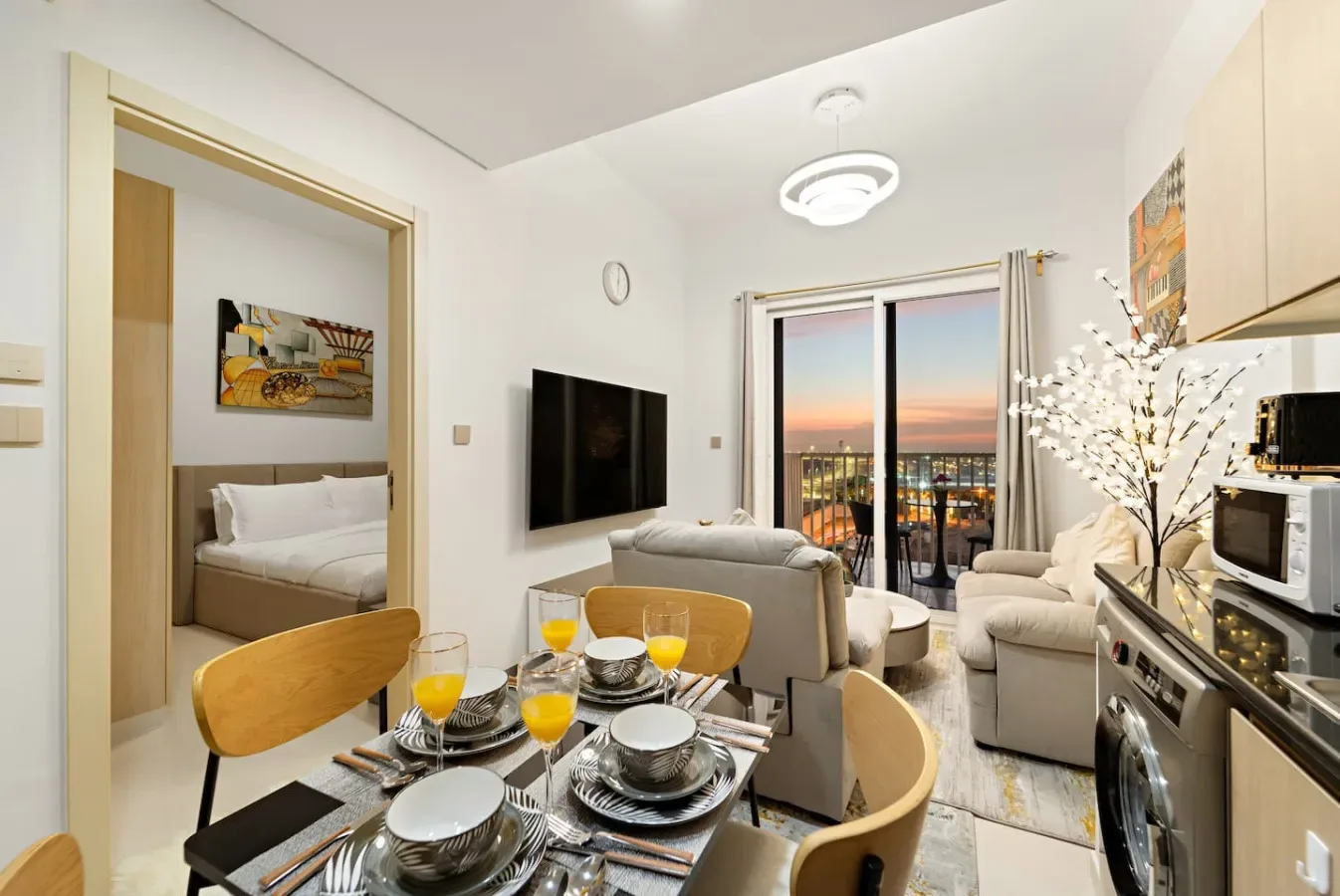 A bright open-plan living and dining area with seating, a set dining table, and balcony doors.