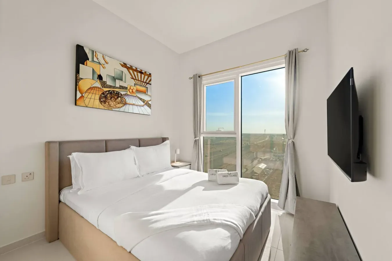 A bright bedroom with a neatly made bed and a large window.