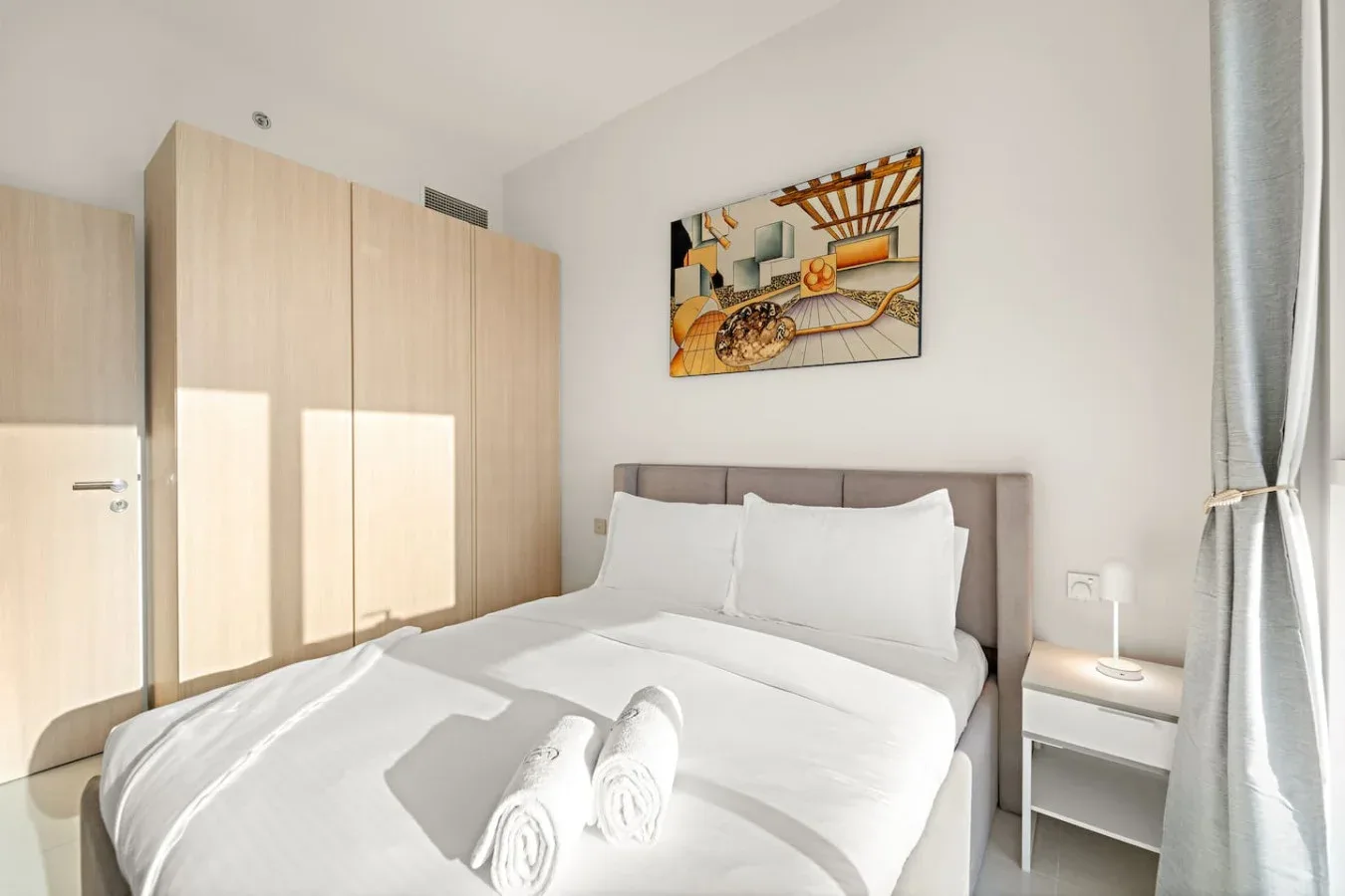 A bright bedroom with a neatly made bed and light wood wardrobes.