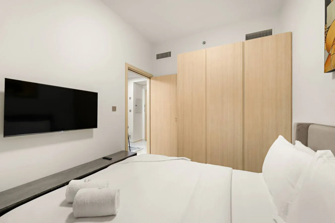A bedroom with a neatly made bed, wall-mounted television, and light wood wardrobes.
