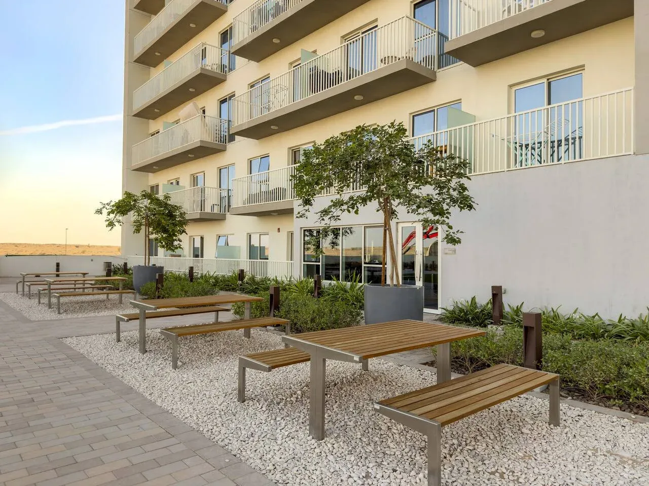 An outdoor seating area with wooden picnic tables beside a modern apartment building.
