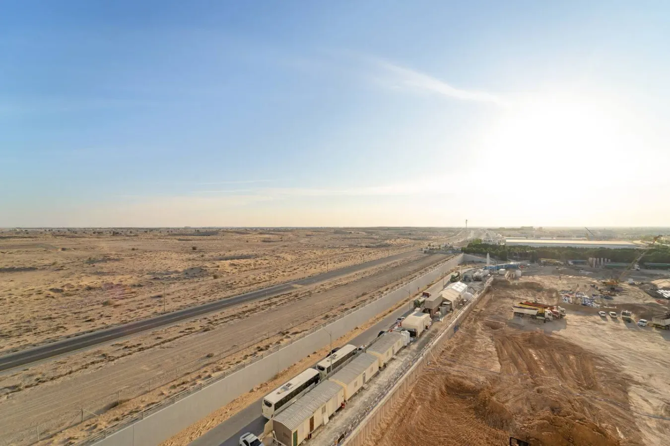 A long train travels through a flat, dry landscape beside a construction site.