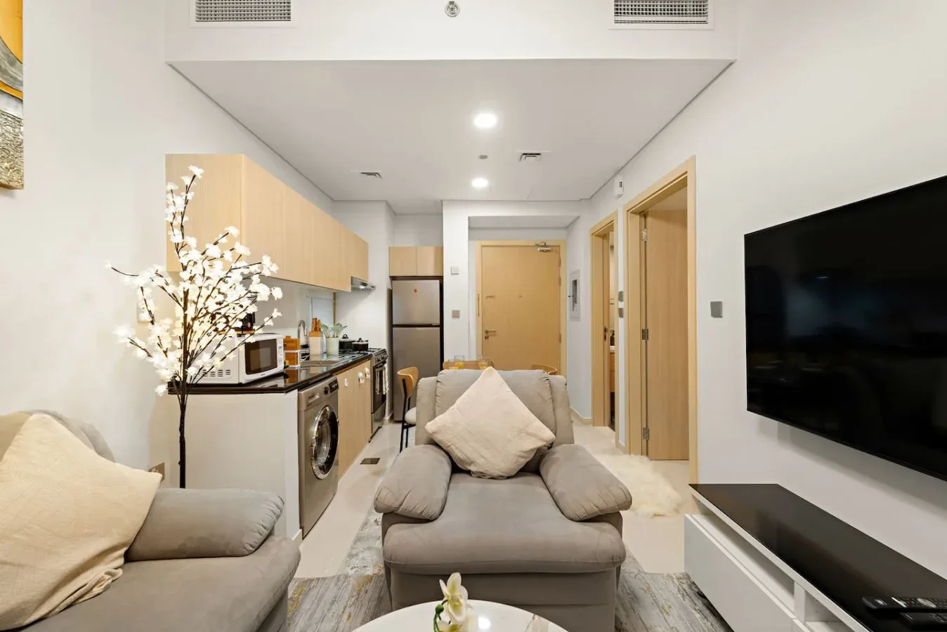 A compact living area with seating, a wall-mounted television, and a kitchenette.