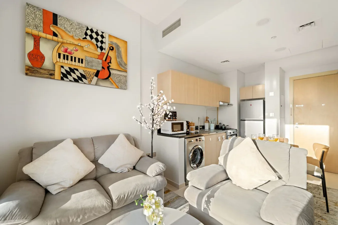 A living room with light-colored seating and a compact kitchen area.