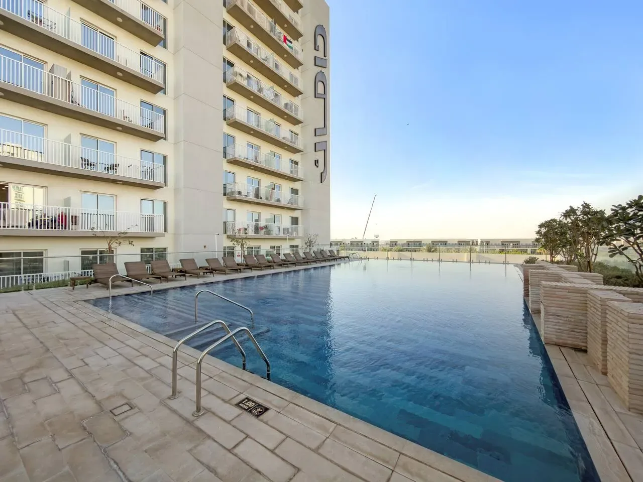 An outdoor swimming pool beside a multi-story building, with seating along the pool deck.