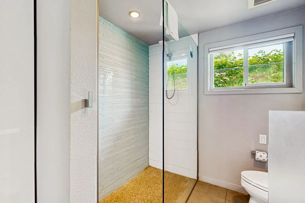 A bright bathroom with a walk-in shower and a window overlooking greenery.
