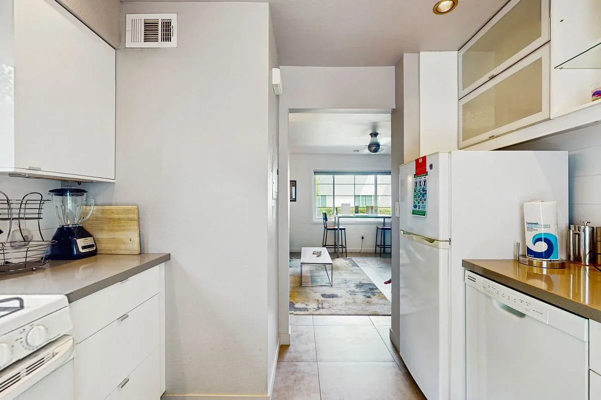 A bright kitchen opens onto a dining area with large windows.