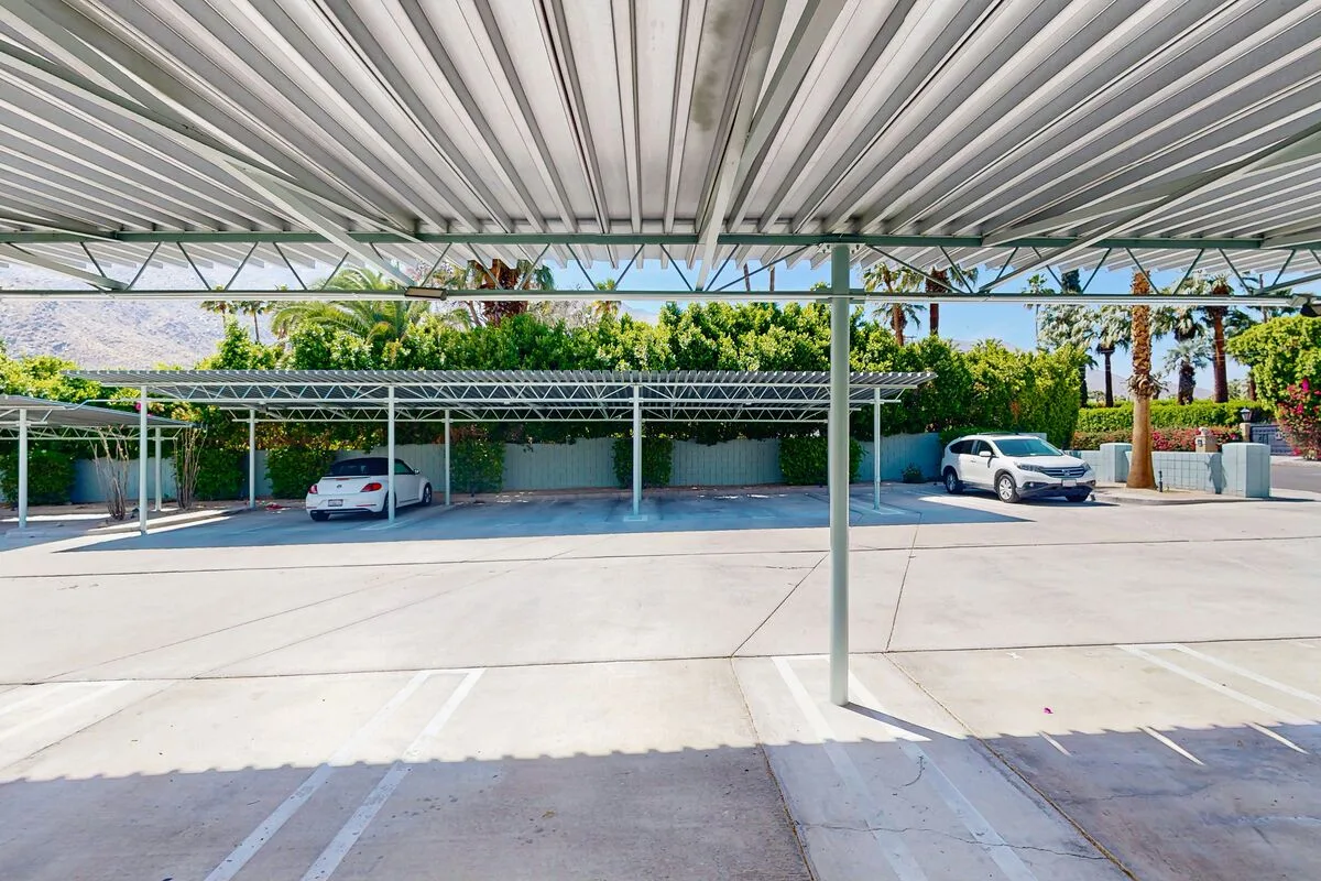 A covered parking area with several parked cars and trees in the background.
