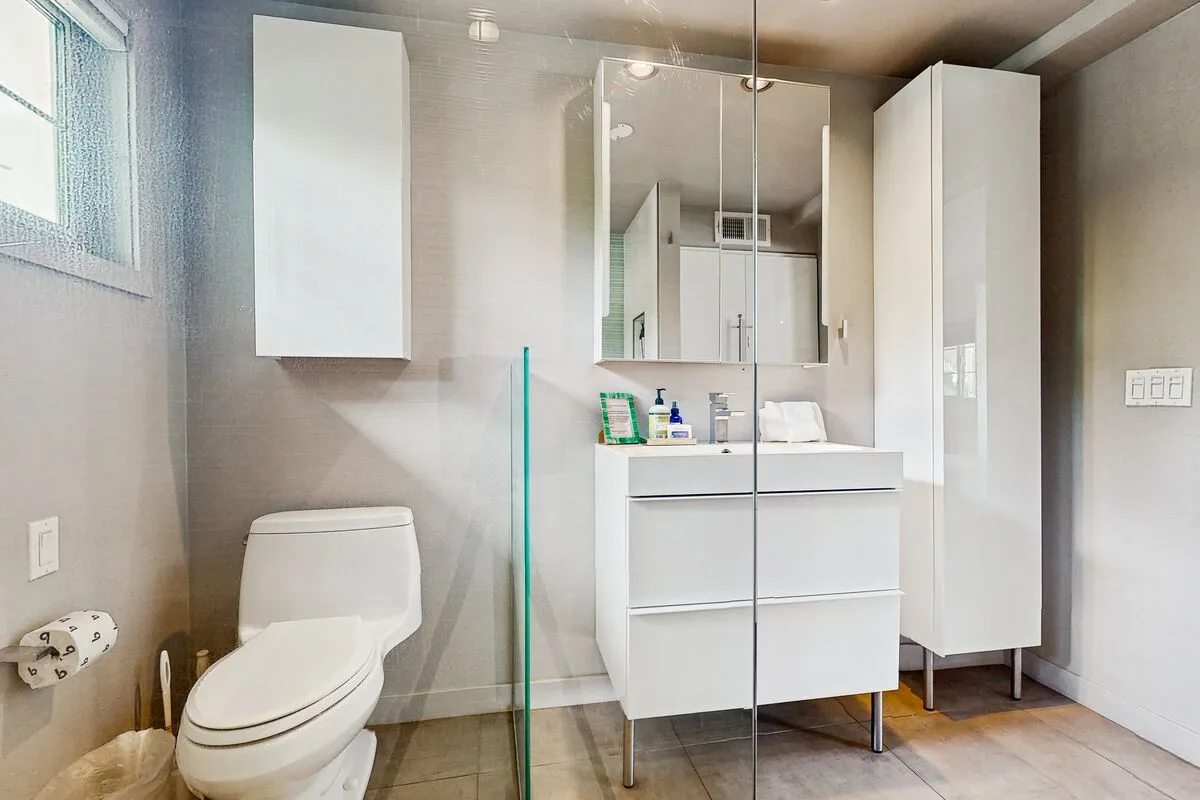 A bright bathroom with a toilet, vanity, and glass shower screen.