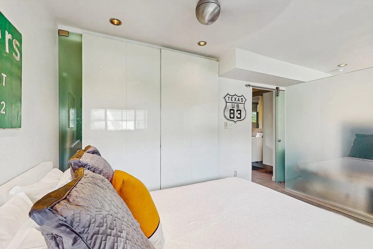 A bright bedroom with a bed, colorful pillows, and white sliding doors.