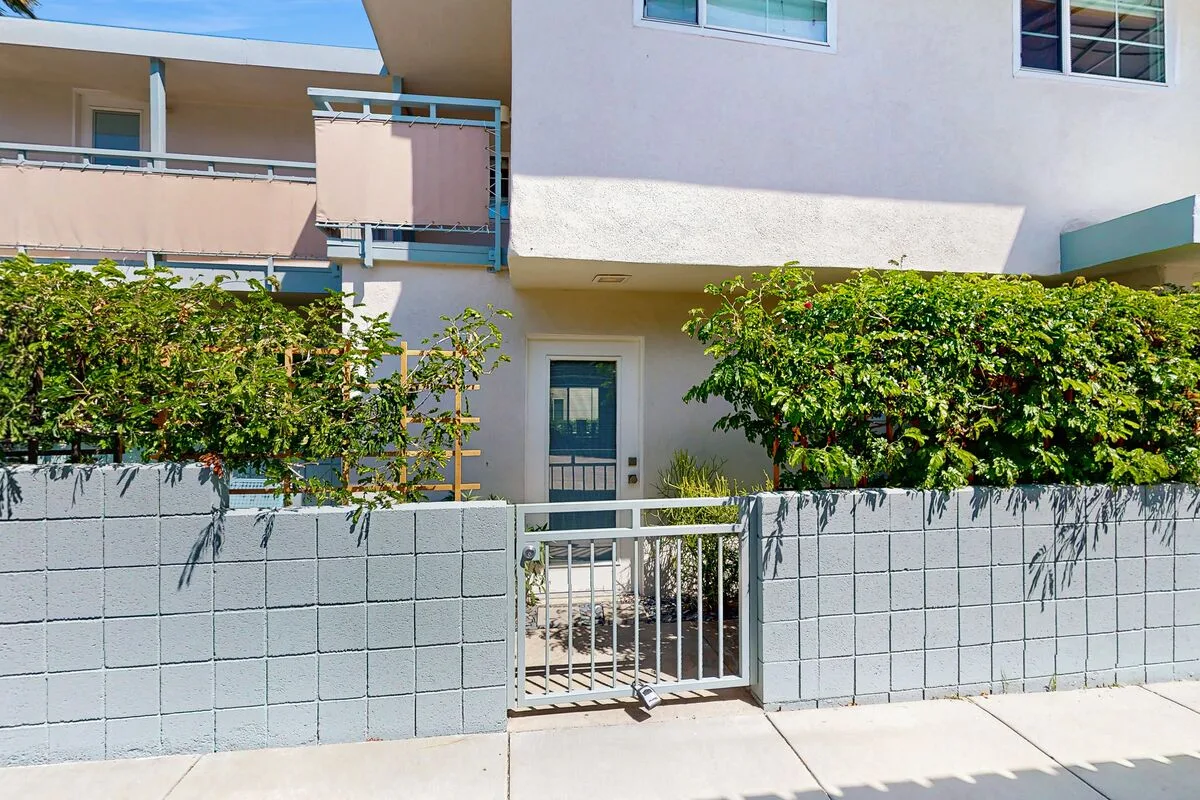 A residential building entrance with a metal gate and leafy shrubs.