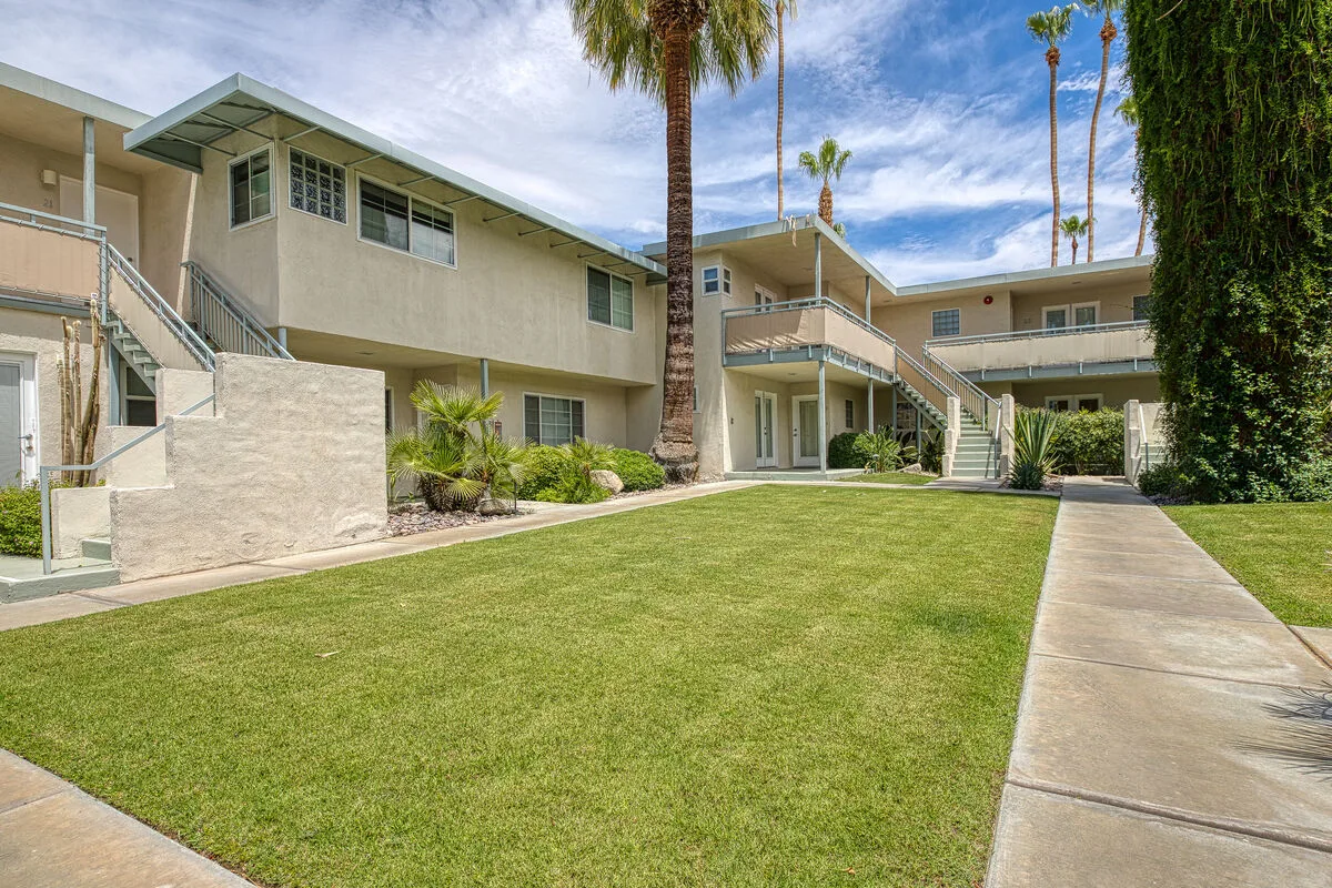 A courtyard lawn and paved walkway sit in front of a low-rise building.