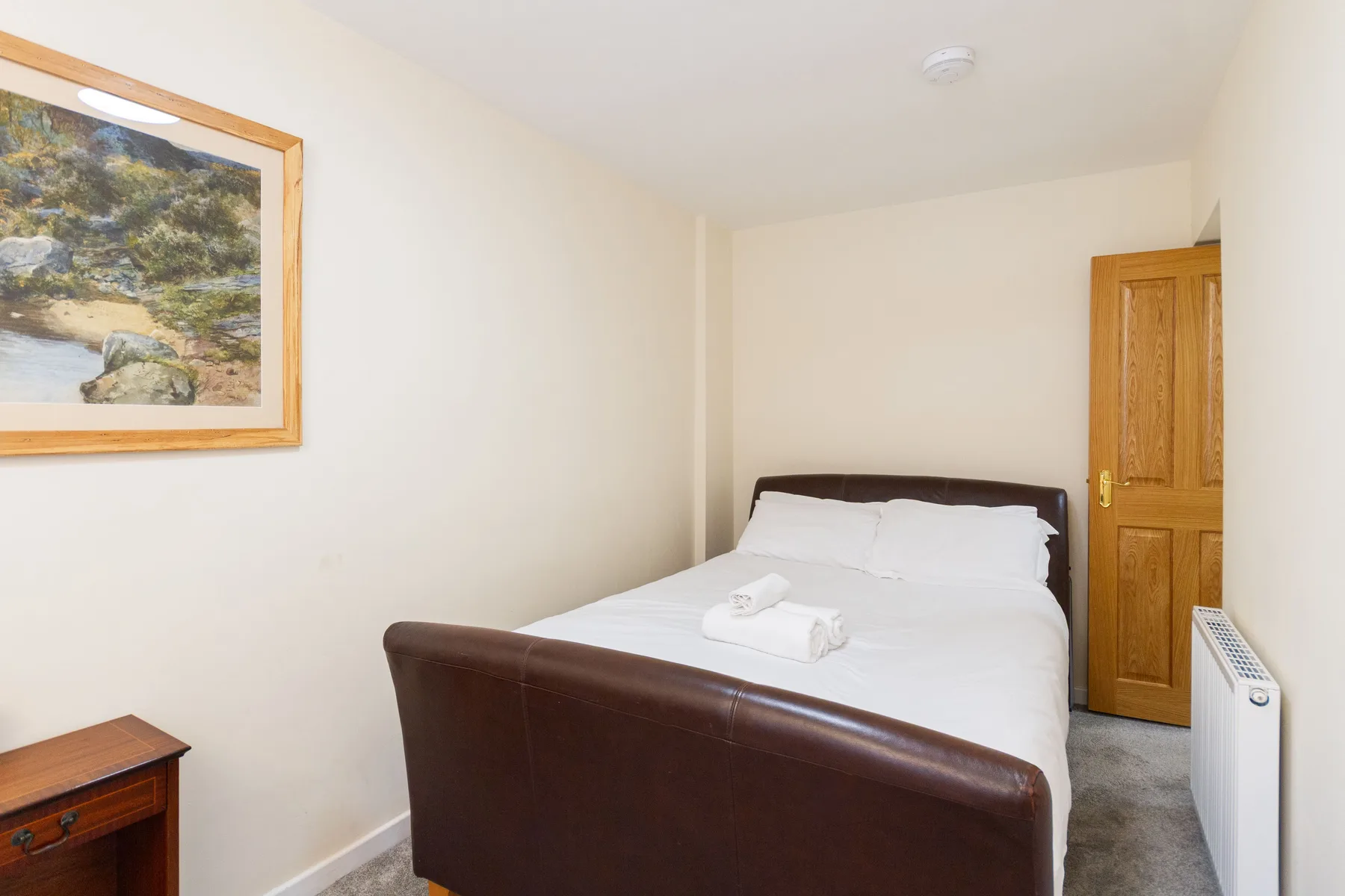 A bedroom with a double bed, framed artwork, and a wooden door.