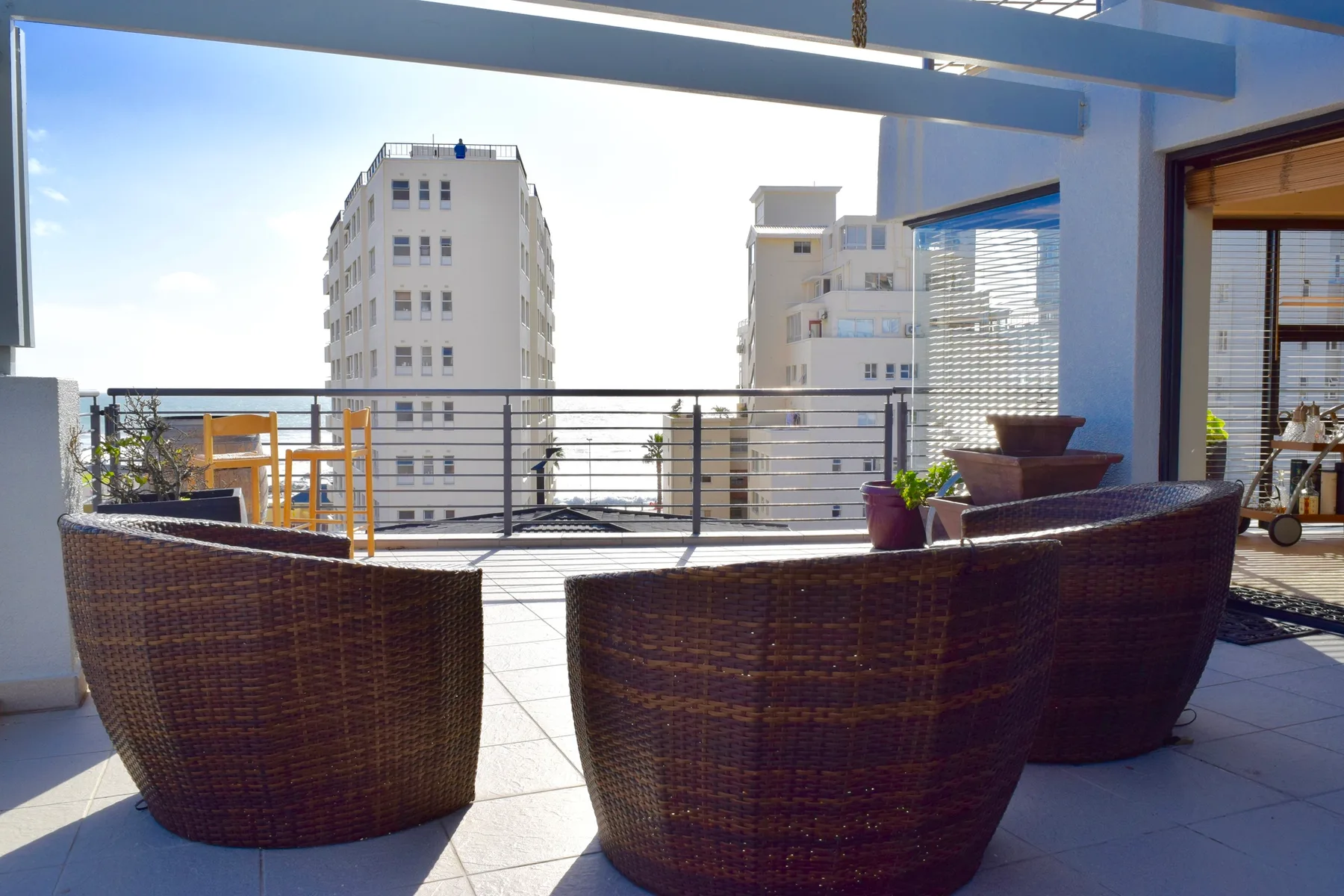 A terrace with woven outdoor seating and a railing overlooking nearby buildings.