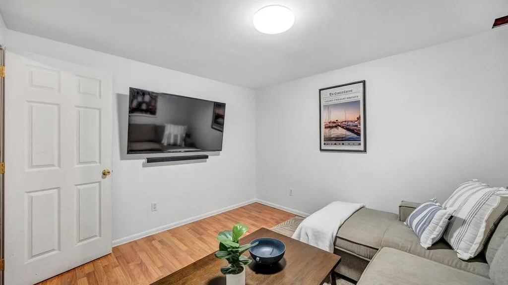 A living room with a wall-mounted television and seating around a coffee table.