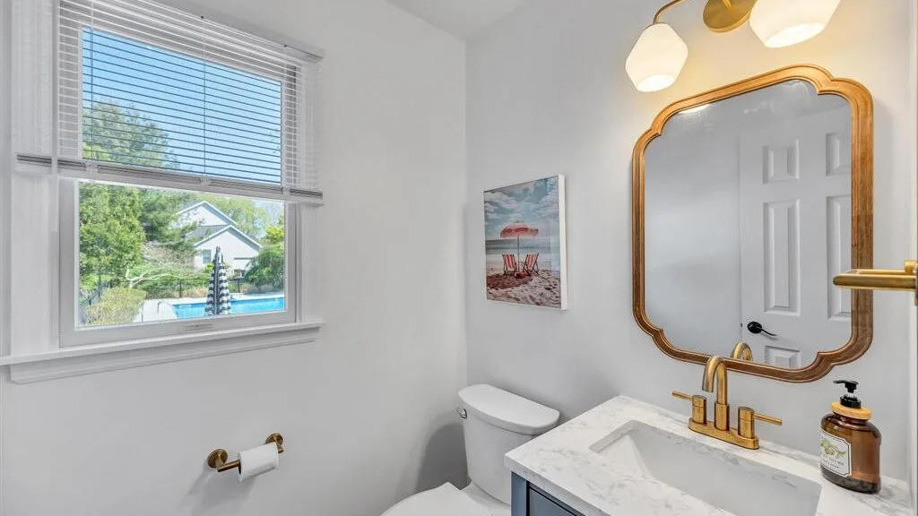 A bright bathroom with a sink, mirror, and window overlooking greenery.