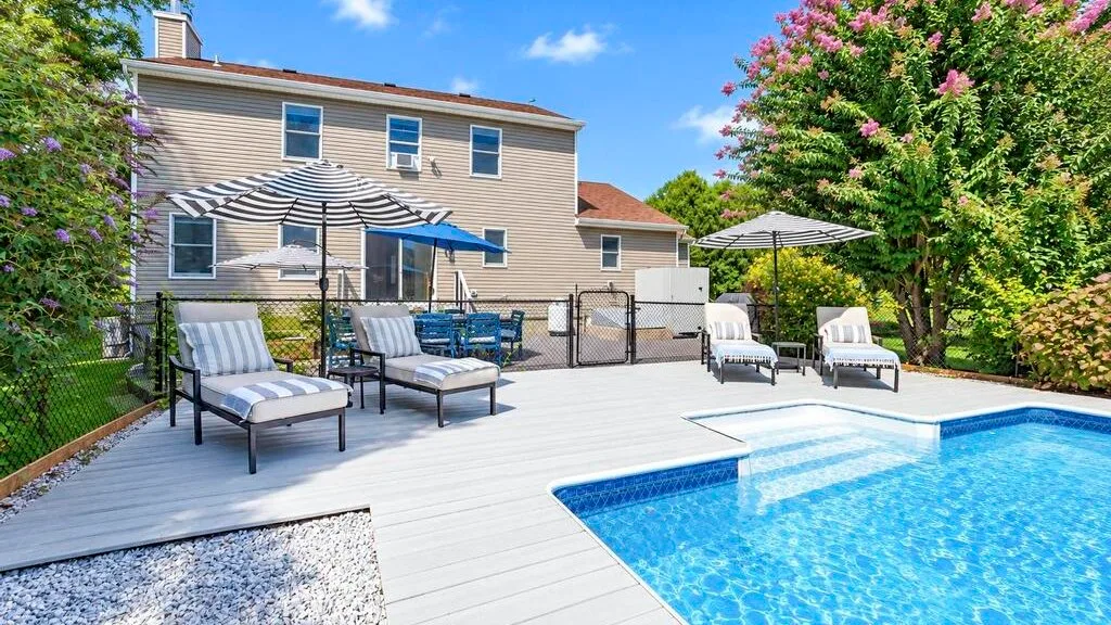 A backyard swimming pool beside a deck with outdoor seating.
