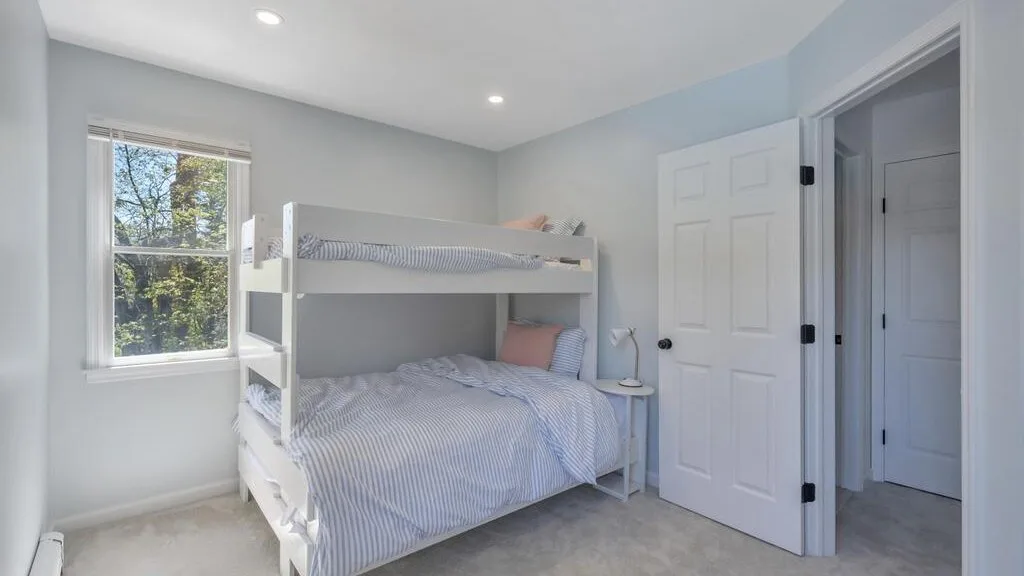 A bright bedroom with a white bunk bed beside a window.