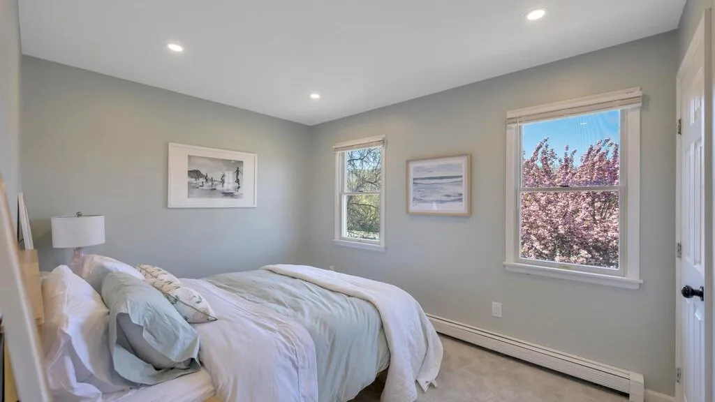 A bedroom with a bed, framed wall art, and windows overlooking trees.