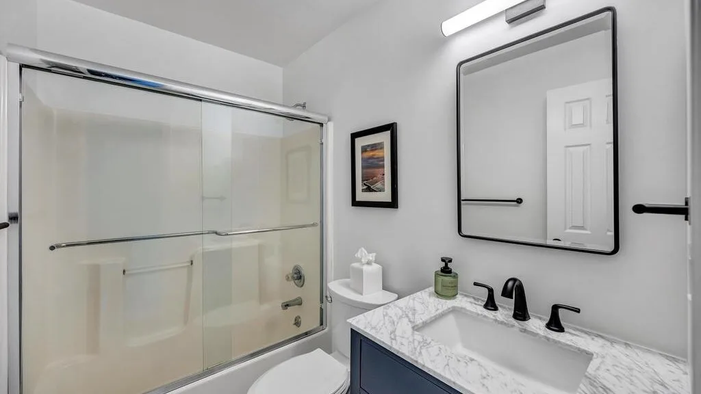 A bathroom vanity with a mirror stands beside a glass-enclosed shower.