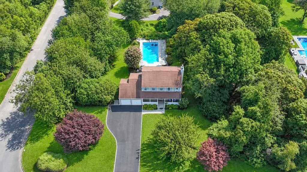An aerial view of a house surrounded by trees, with a swimming pool behind it.