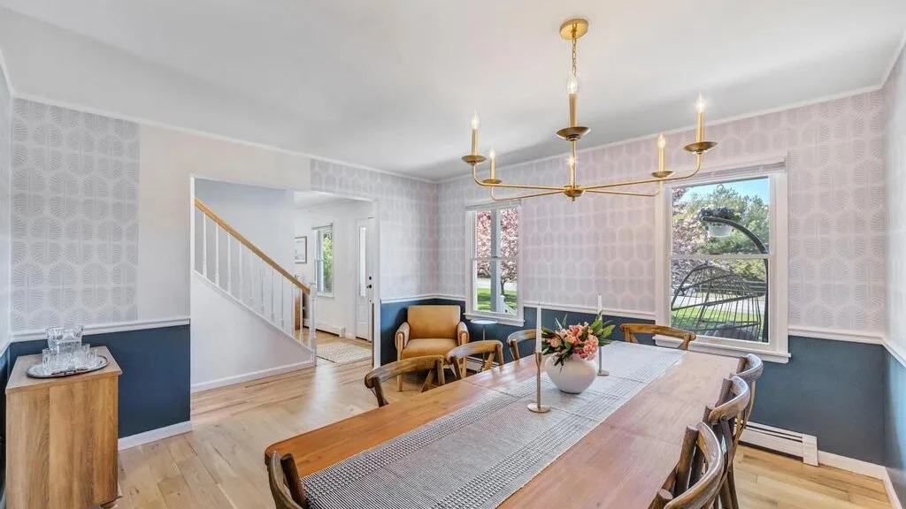 A dining room with a long table, chairs, and windows overlooking greenery.