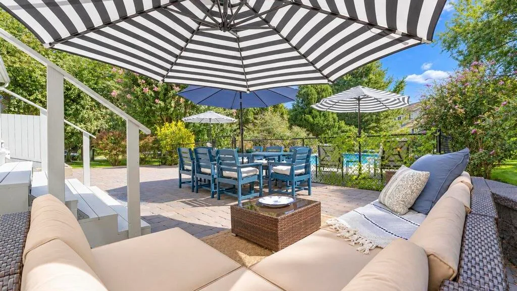 A furnished outdoor patio has seating, a table, and striped umbrellas.