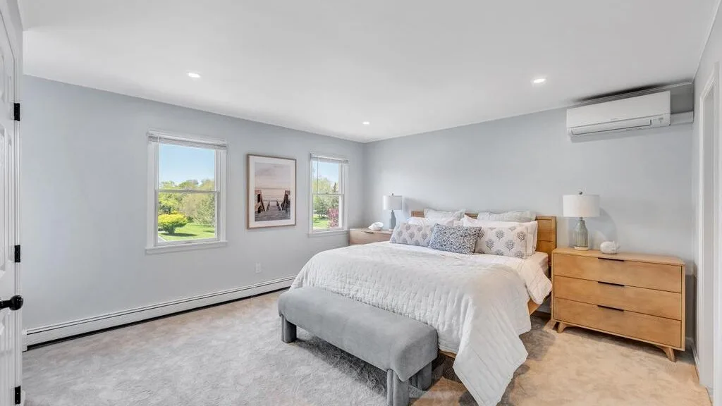 A bright bedroom with a bed, upholstered bench, and windows.