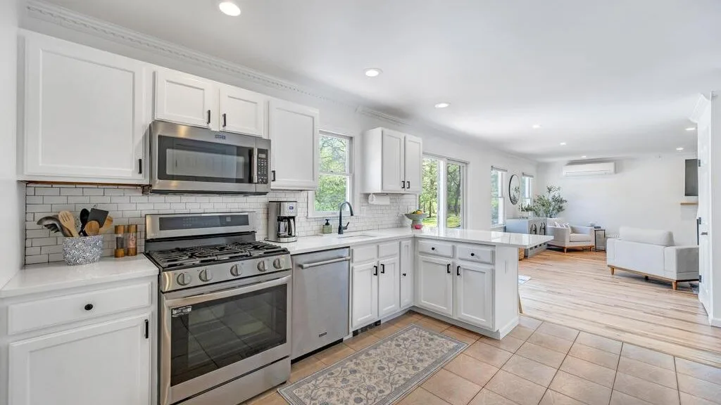 A bright kitchen opens into a living area with light-colored seating.